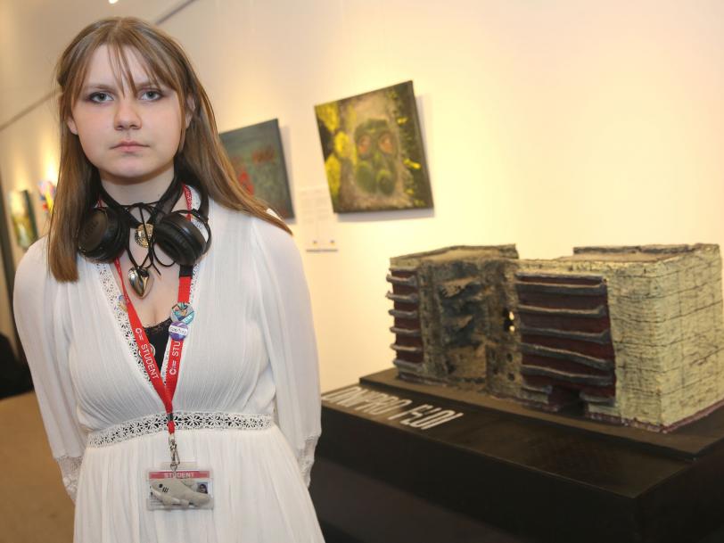 A young women in front of her artwork, a model of a destroyed tower block in Dnipro.