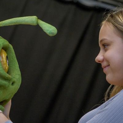Photo of a girl holder a green puppet.