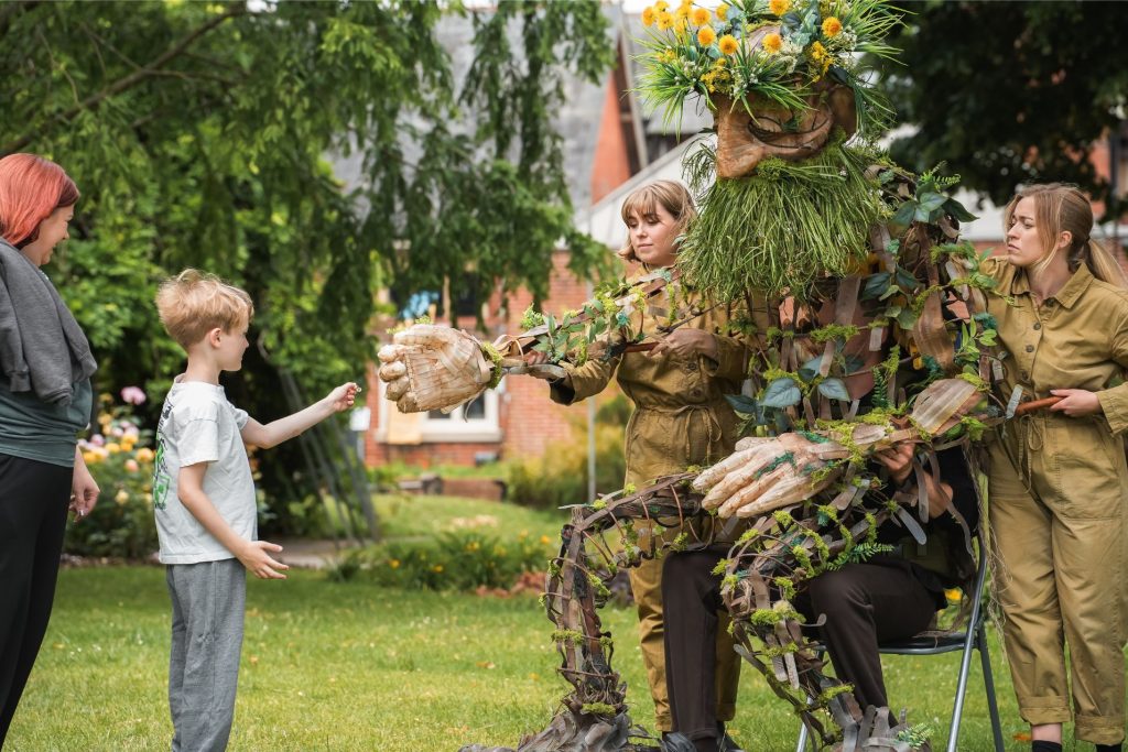 A giant dandelion man puppet reaches out to boy