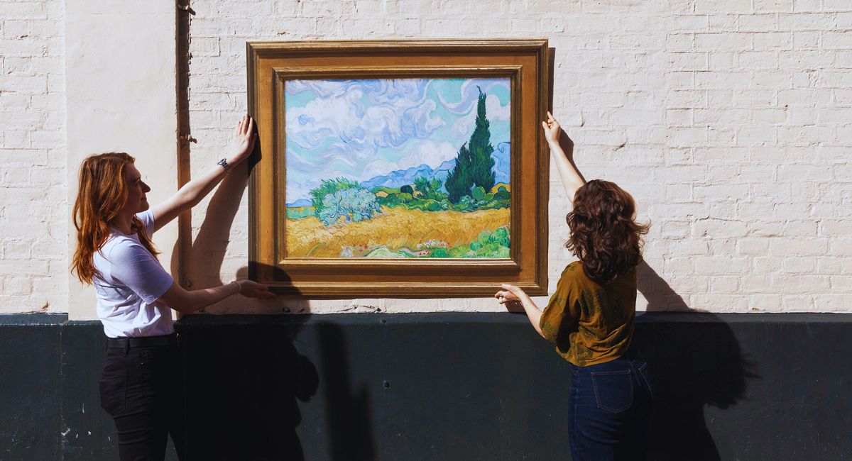 Two people hanging a framed painting on a wall