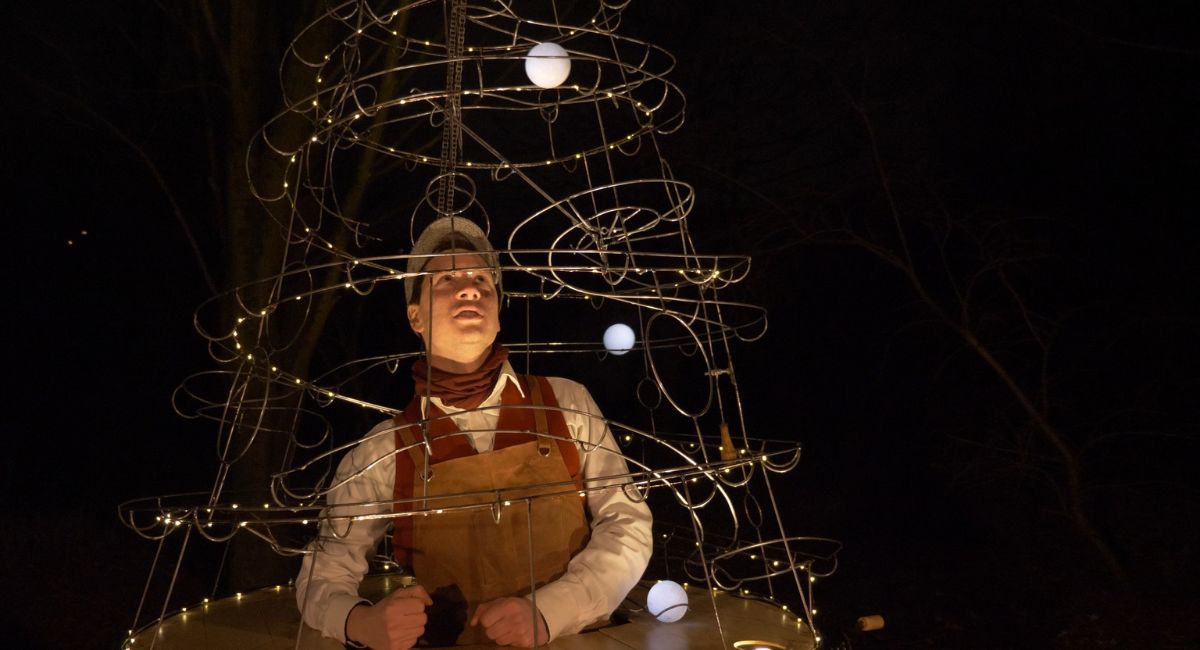 A man inside a light up Christmas tree sculpture