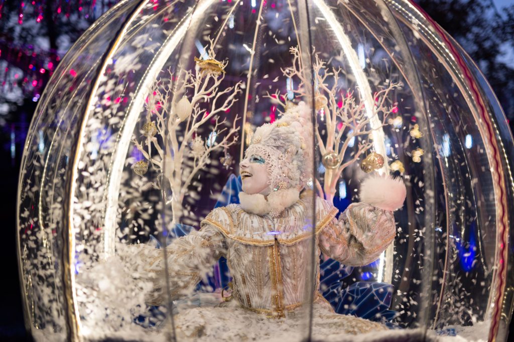 The Snow Queen in an elaborate white and gold costume inside a giant magical snow globe