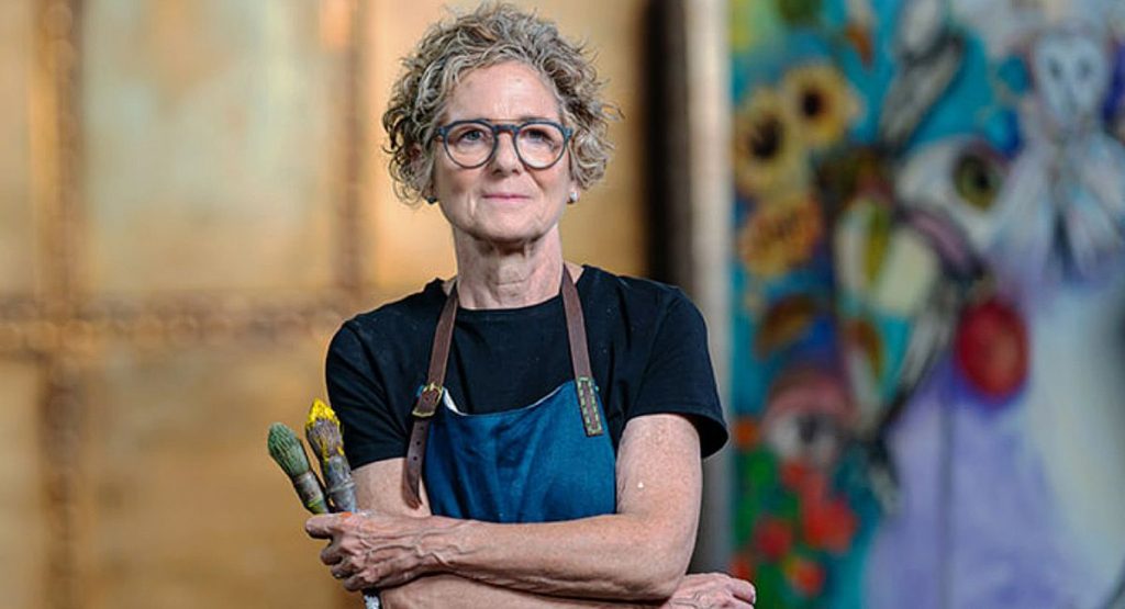 Visual artist Rachel Gadsden wearing an apron and holding her paint brushes