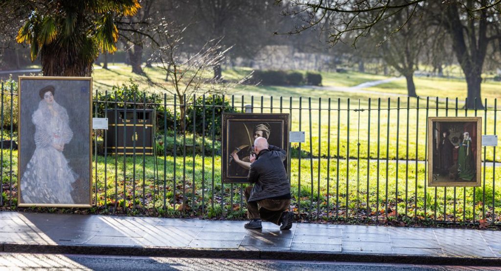A series of gold framed paintings on the railings outside a park in Croydon.