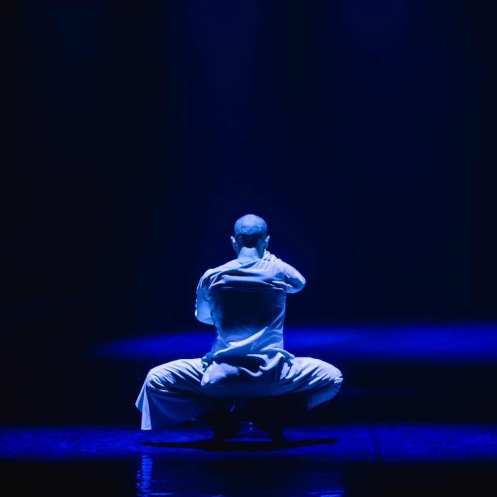 A blue lit figure crouches on a stage