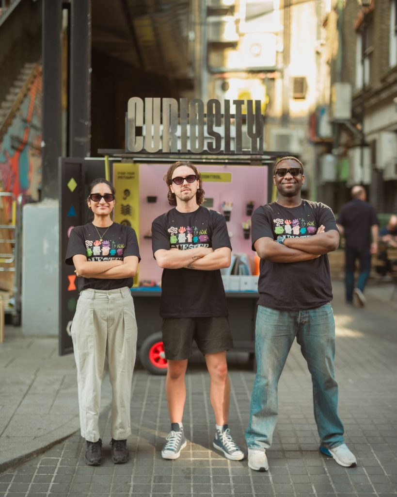 Three creative facilitators stand in front of the Rover in black sunglasses